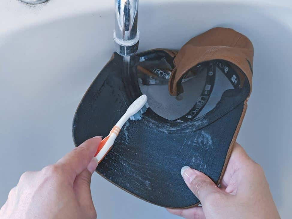 man using toothbrush to clean baseball cap