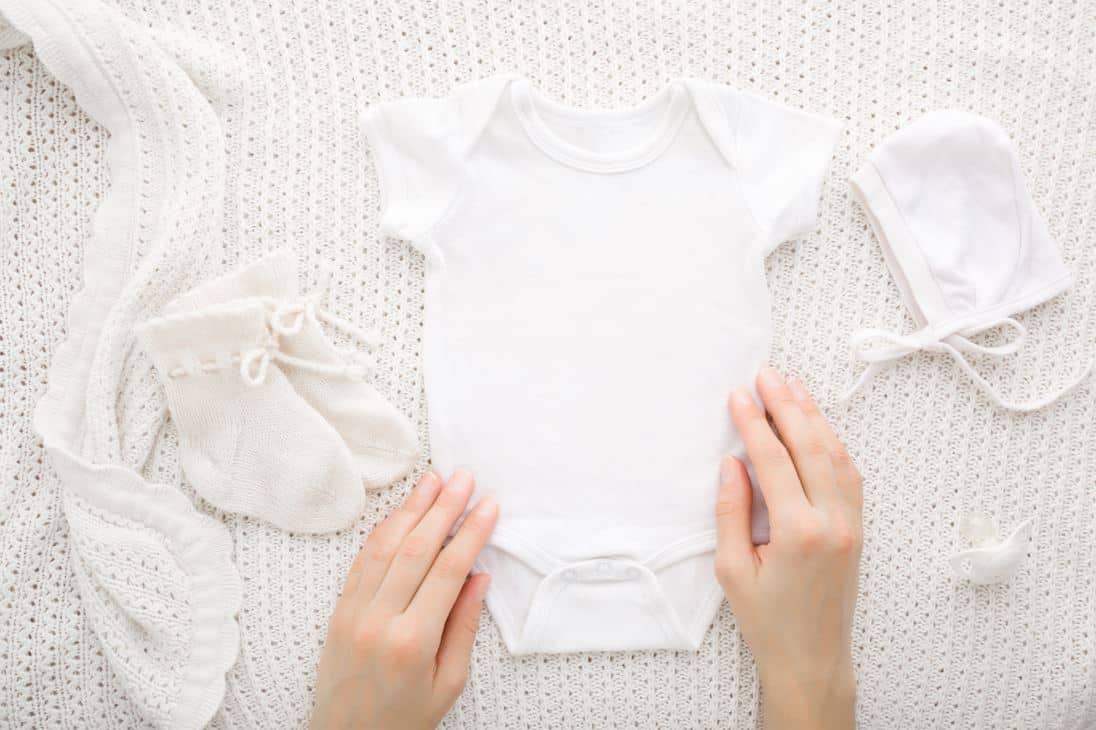 woman folding white baby romper