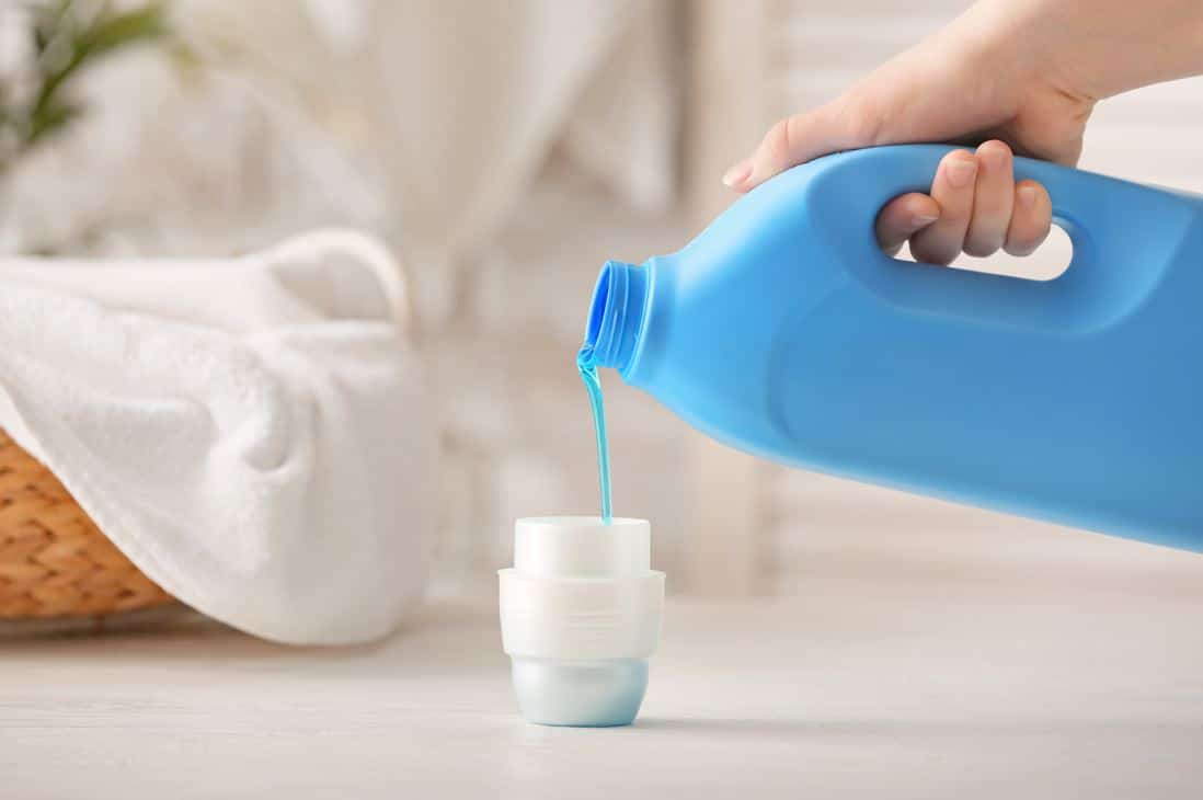 woman measuring out blue fabric softener into a white lid