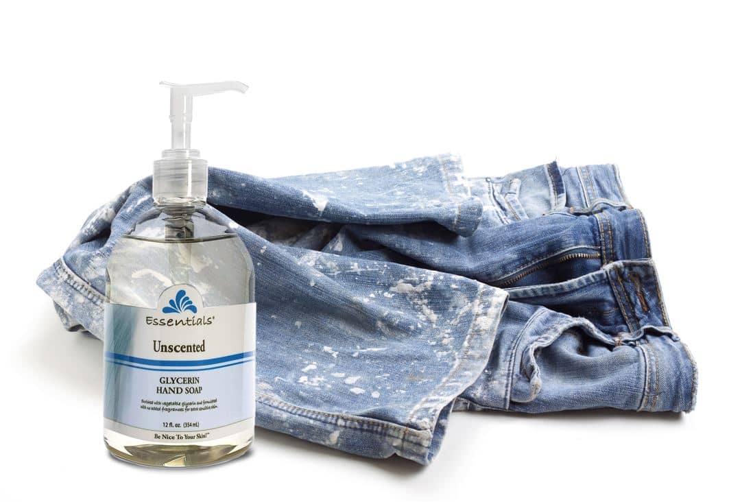 bottle of unscented glycerin soap next to blue jeans that are soiled from white paint