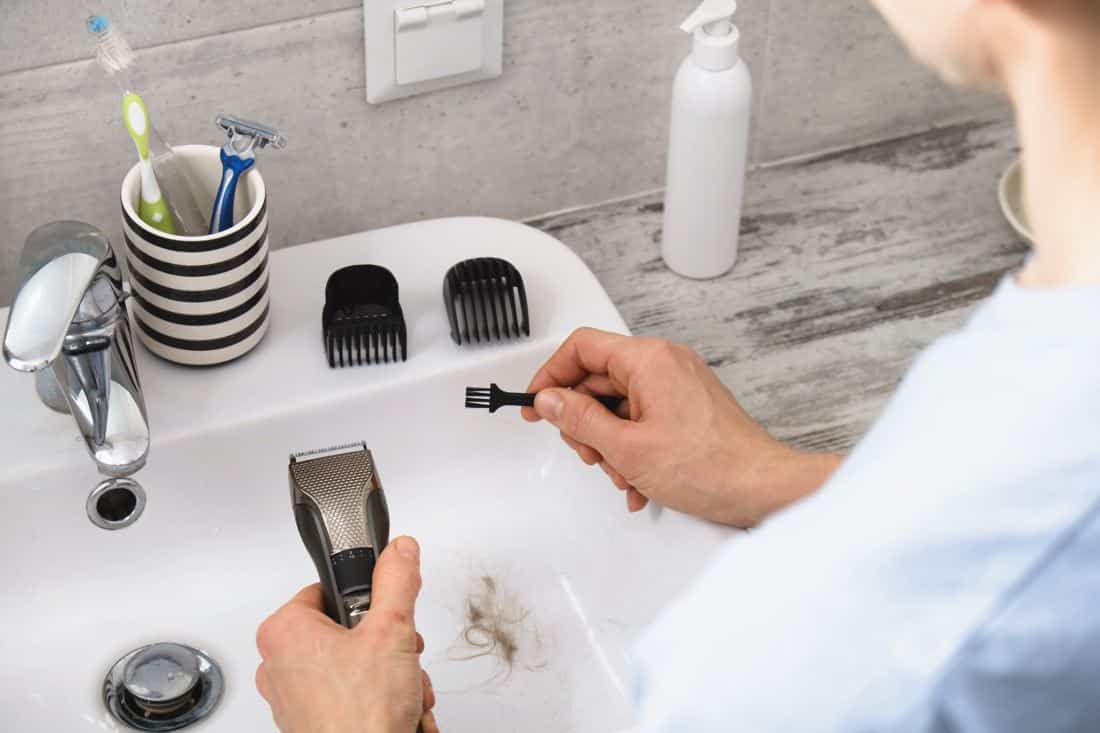 man cleaning handheld shaver using a small brush next to a white porcelain sink