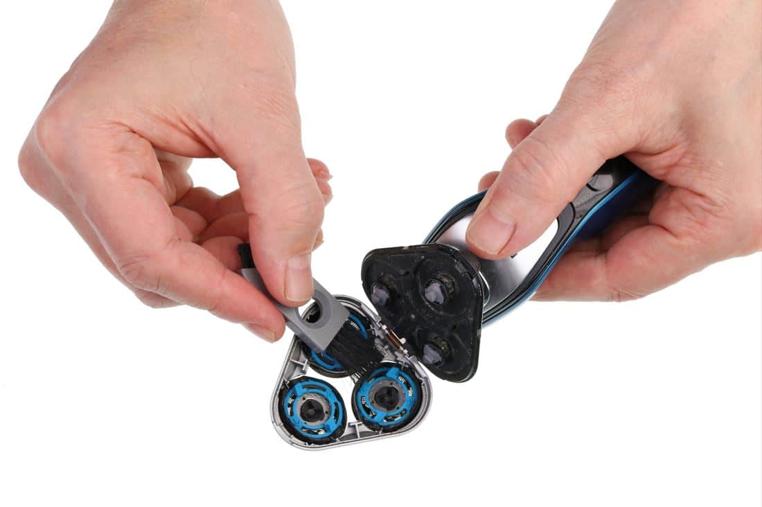 man using small brush to clean internal components of an electric shaver