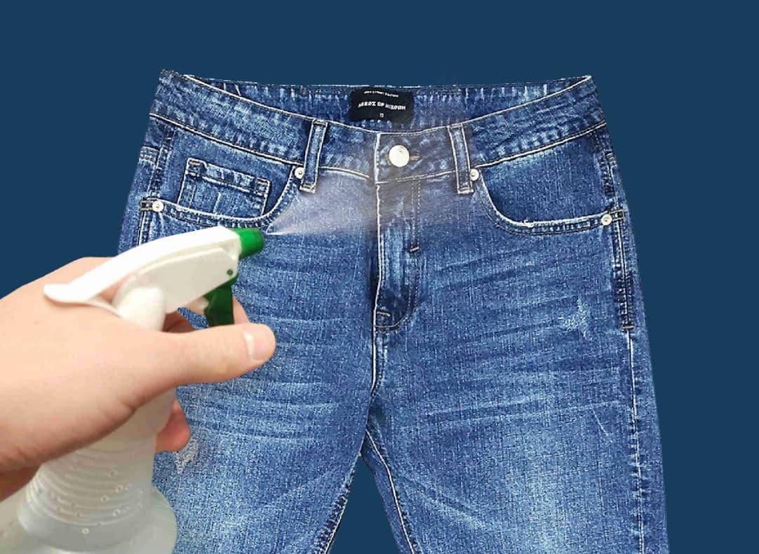person using spray bottle to spray clear solution on blue denim jeans