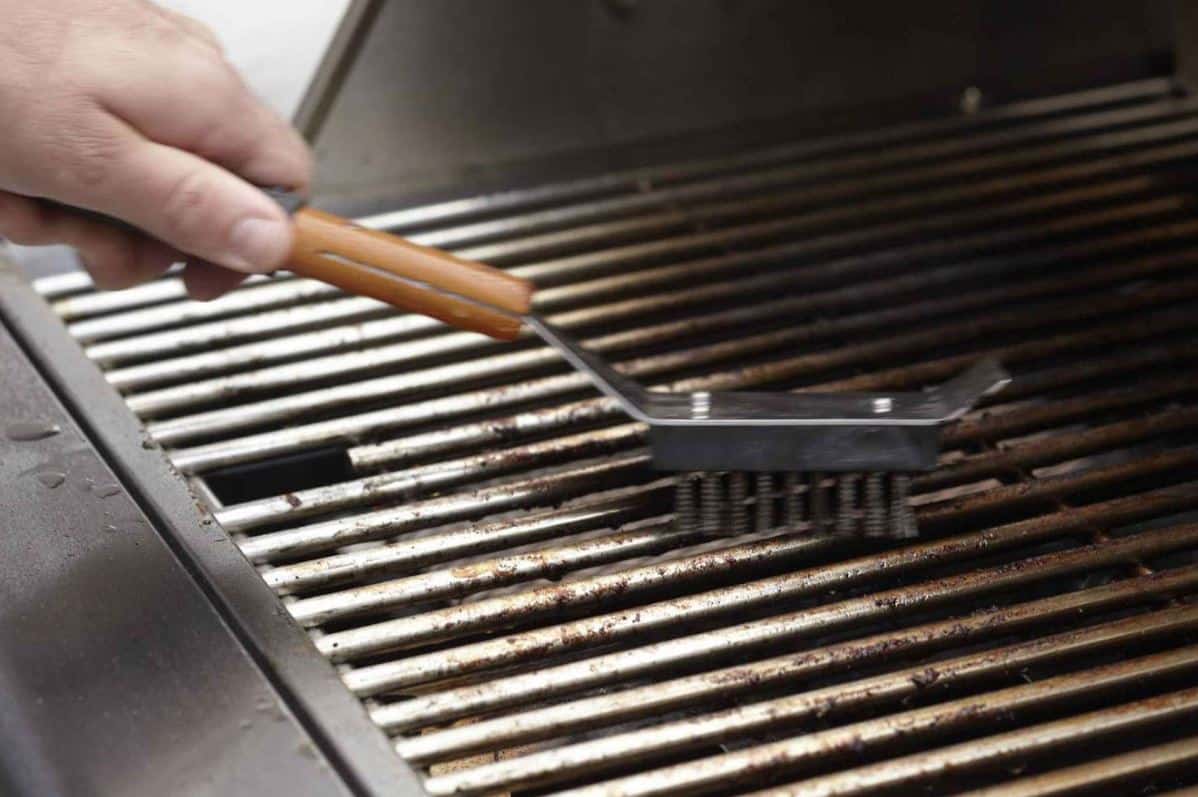man cleaning dirty bbq tubes with a steel brush