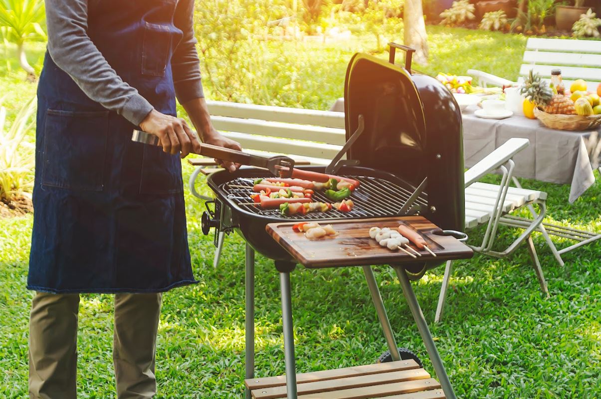 man cooking sausages and vegetable kebabs on weber q