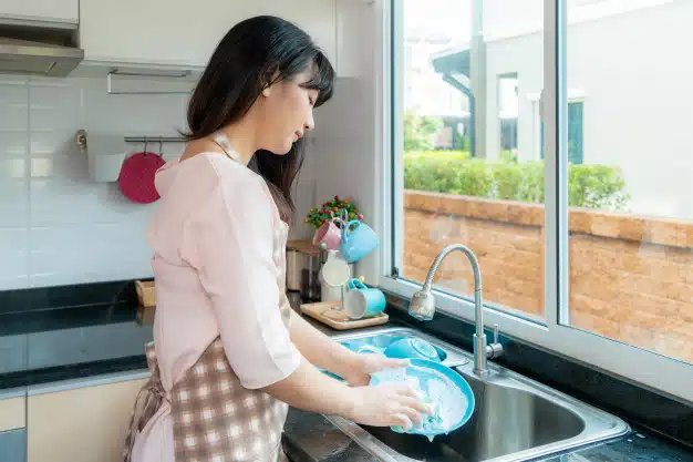 attractive-young-asian-woman-is-washing-dishes-kitchen-sink-while-doing-cleaning-home-during-staying-home