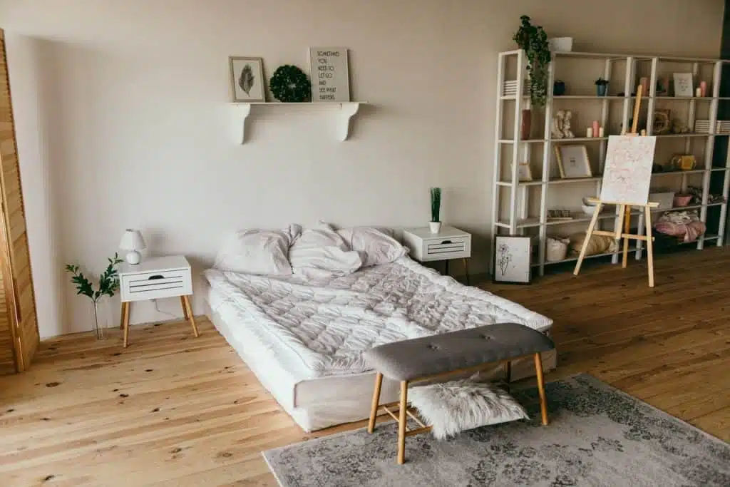 A bedroom with a white wooden shelf beside the bed