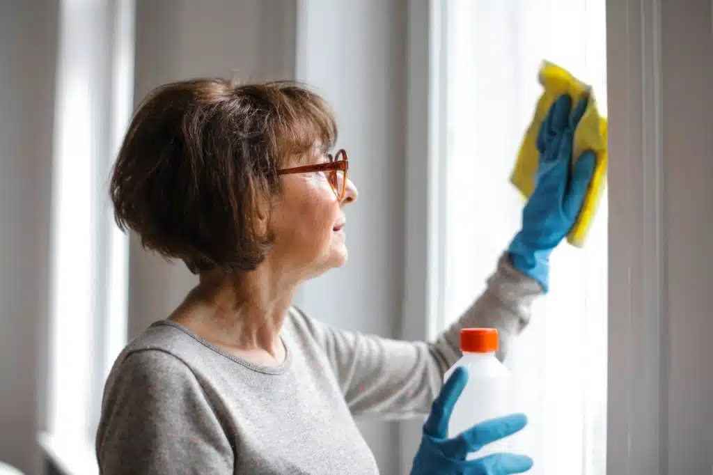 Older cleaning lady wearing gloves cleaning a window with a sponge