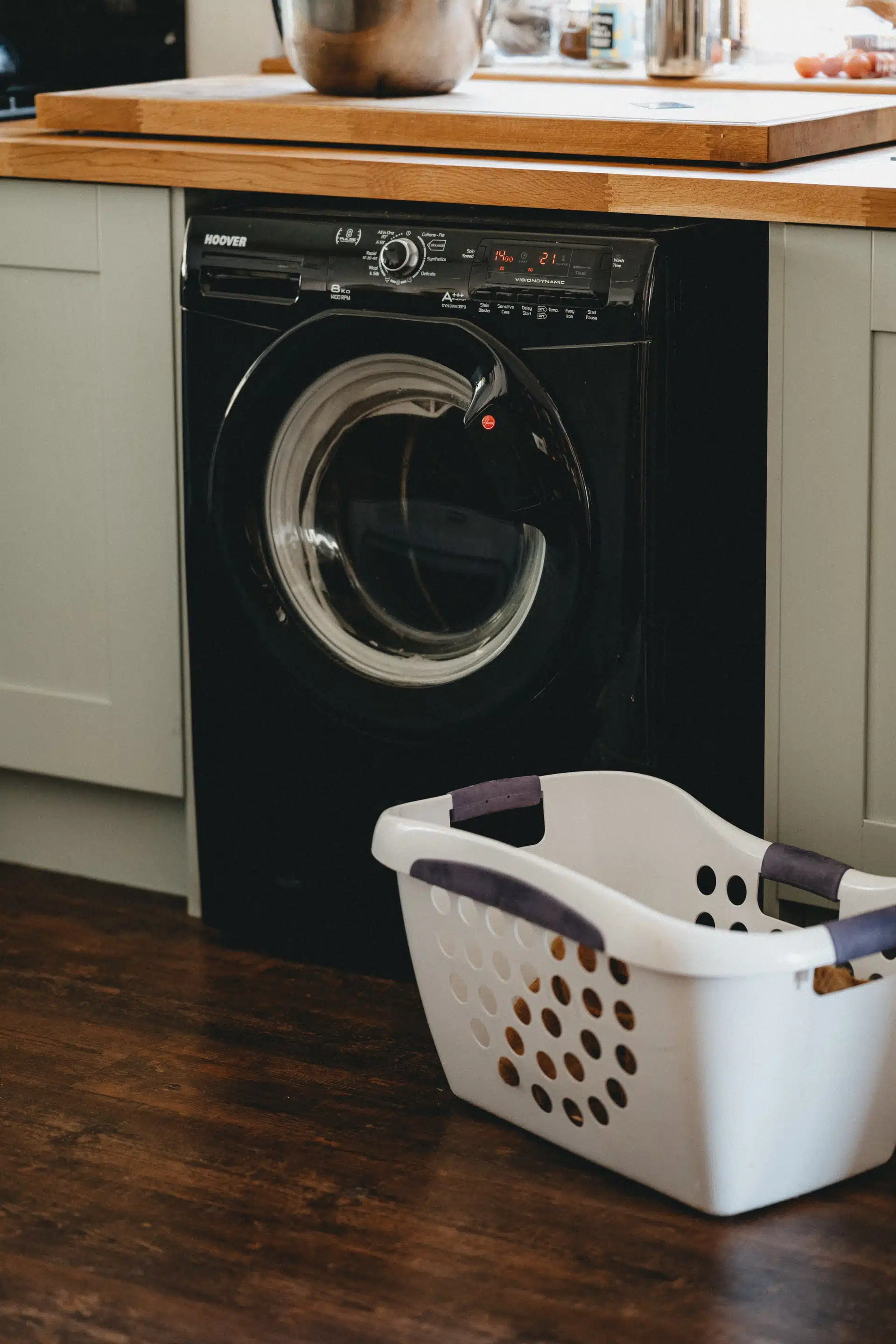 Black washing machine under a wooden cabinet
