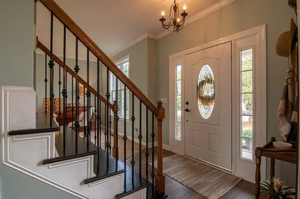 An entryway of a house with a Brown wooden staircase with brass chandelier