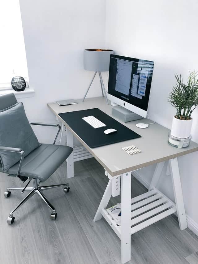 A home office with a macbook,a black chair and a grey office table
