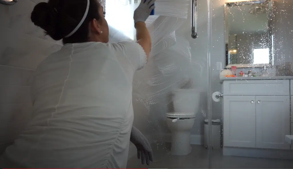 A woman removing lime scale from a shower screen