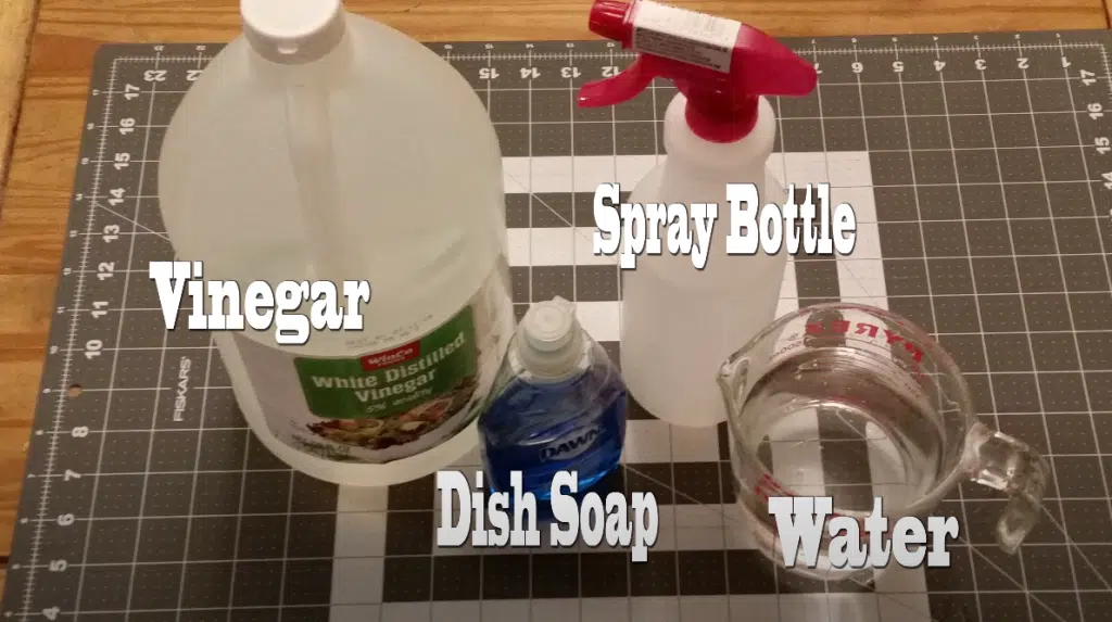 A bottle of vinegar, a spray bottle, a bottle of dishwasher soap and a pitcher of water placed on a table