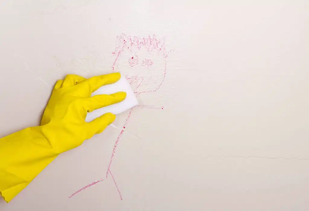 Person with yellow rubber glove cleaning drawing on wall