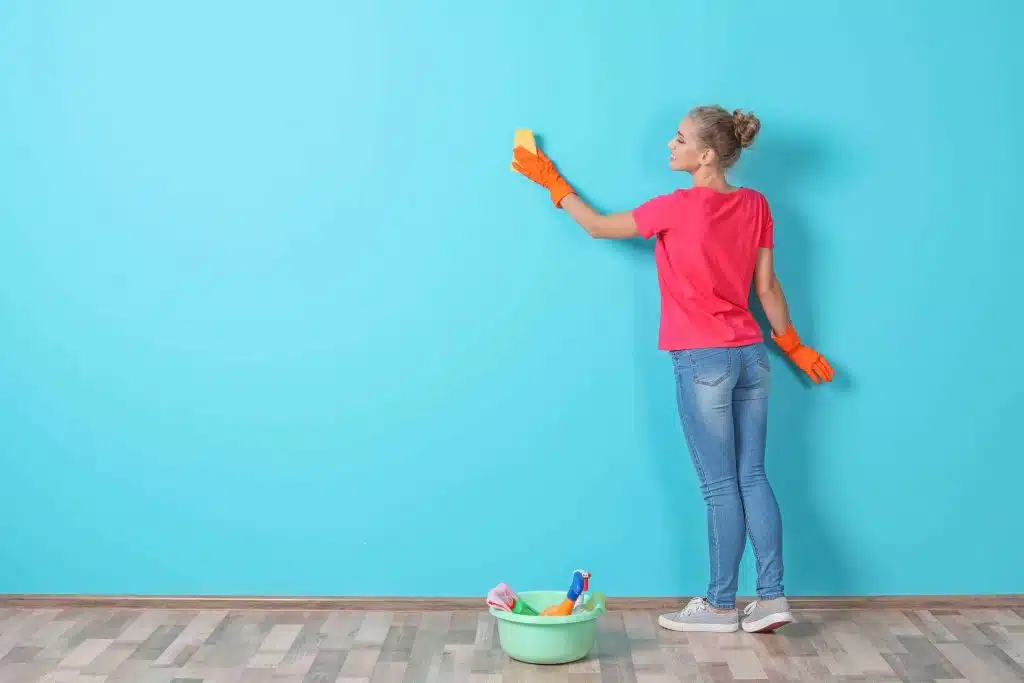 Woman in red t-shirt facing a blue wall cleaning it.