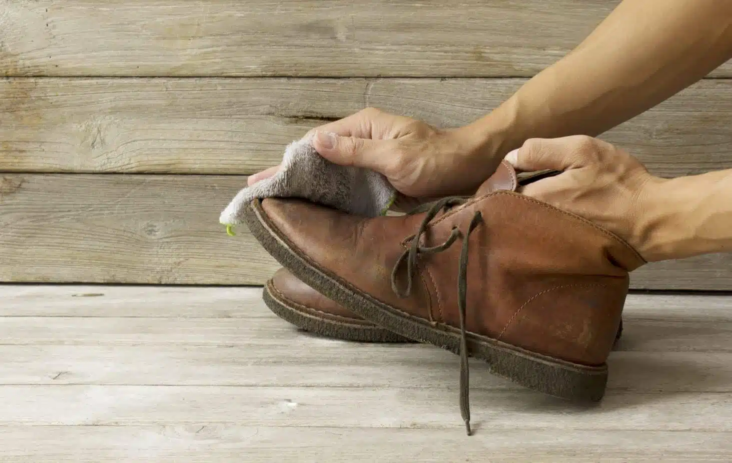 A man cleaning worn brown leather boots by hand
