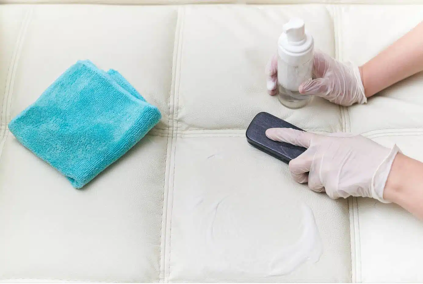 person cleaning a white leather couch with a blue cloth and detergent