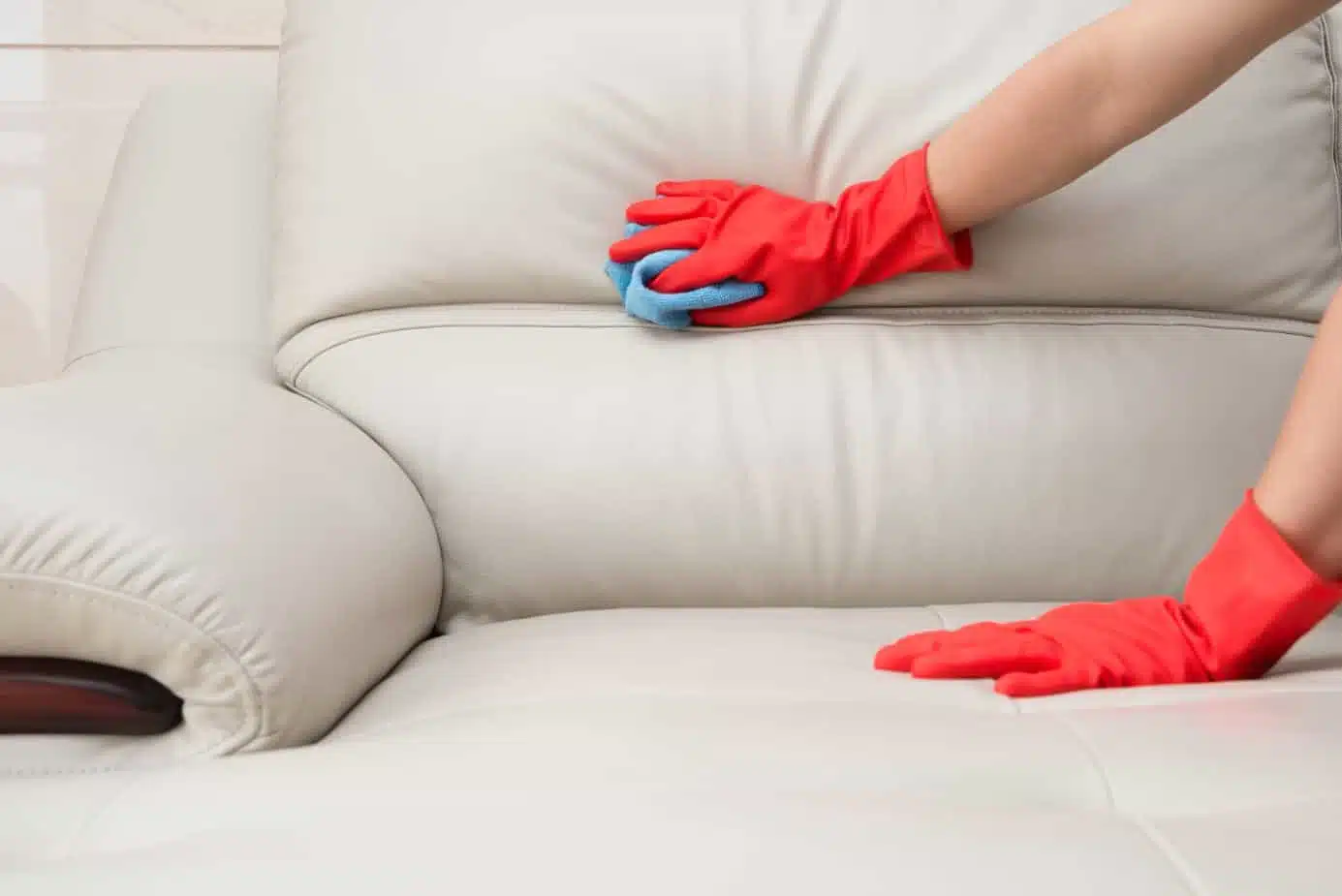 person cleaning white leather couch with a blue cloth