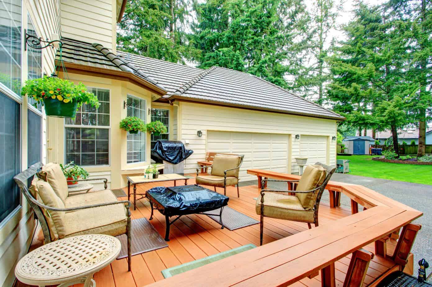 antique patio furniture on a light brown wooden deck in a large backyard