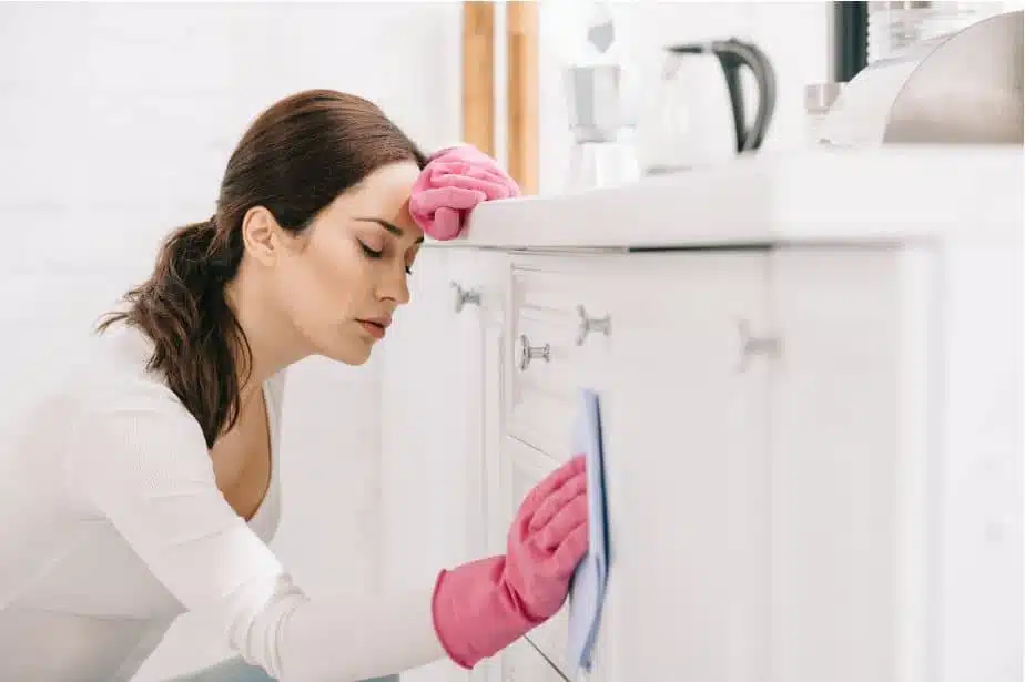 tired woman cleaning the outsides of a kitchen cabinet