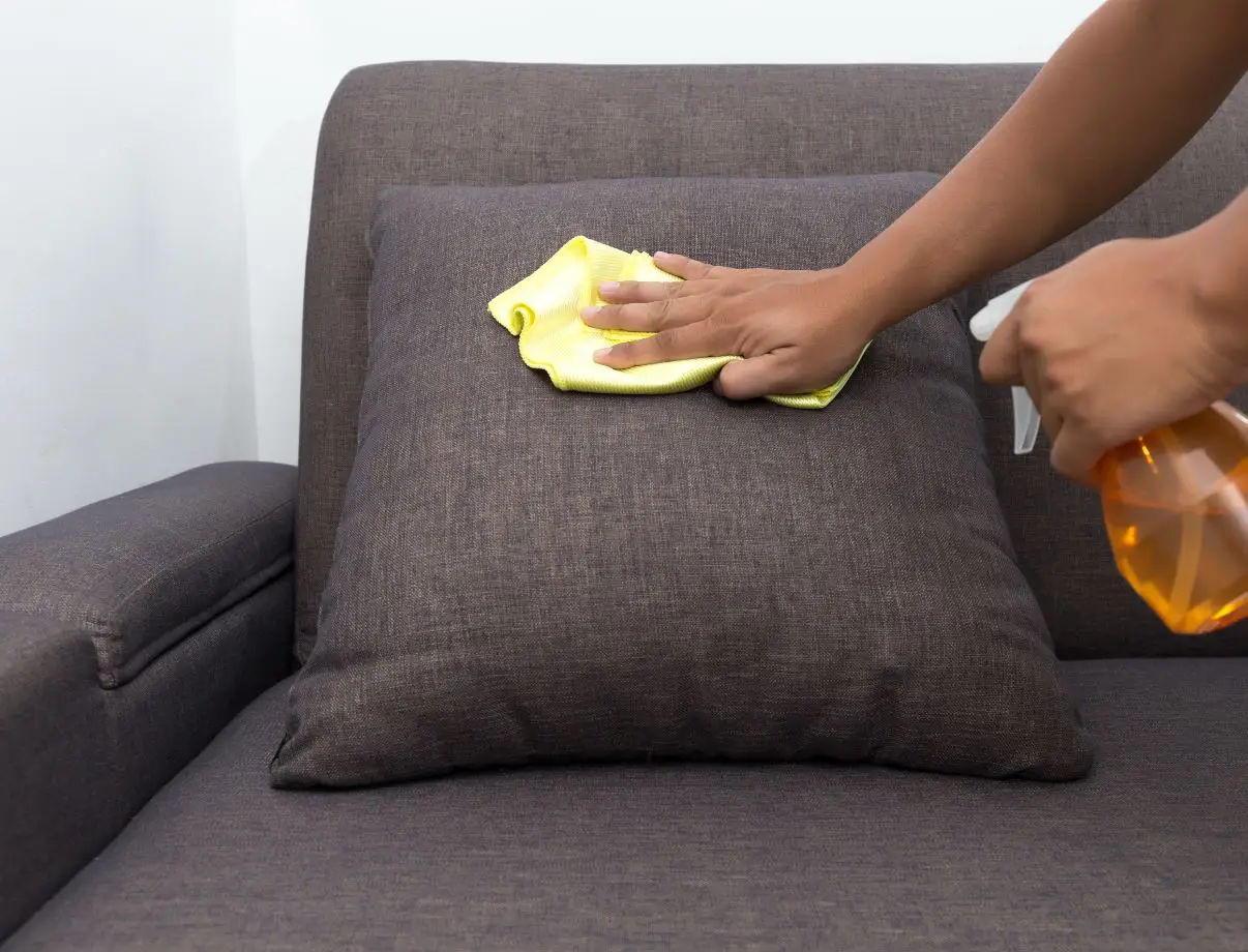 person scrubbing upholstered pillow with a cleaning solution
