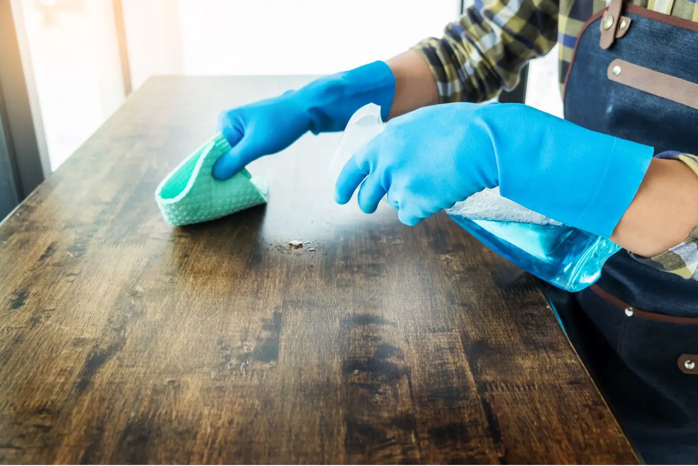 lady with blue gloves cleaning wooden table with green rag