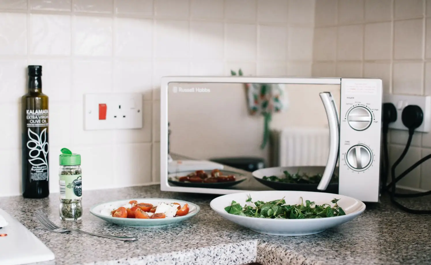white russell hobbs microwave on a benchtop with a plate of feta and cherry tomatos in the front