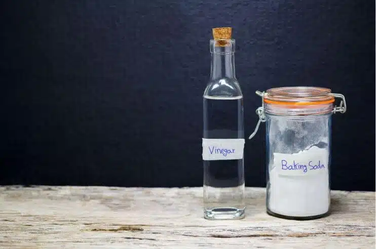 bottle of vinegar and a full jar of baking soda on a wooden bench