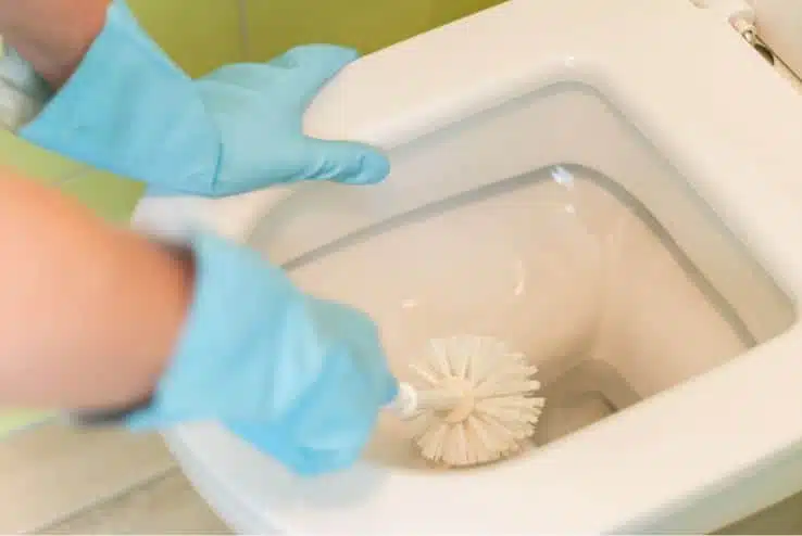 person with blue gloves scrubbing water stained white porcelain toilet