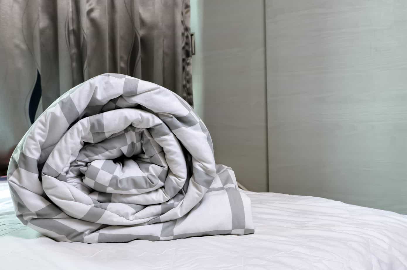 checkered white and grey duvet folded on a bed with white sheets