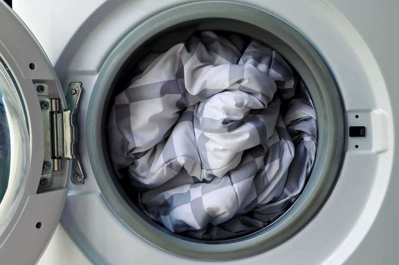 checkered white and grey duvet fully loaded into a white front loader washing machine ready to be washed