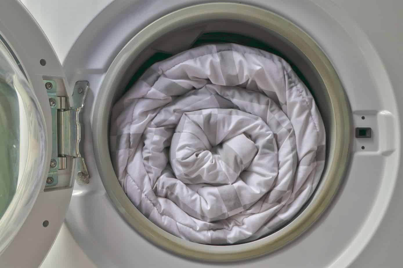 checkered white and grey duvet fully loaded into a white front loader washing machine