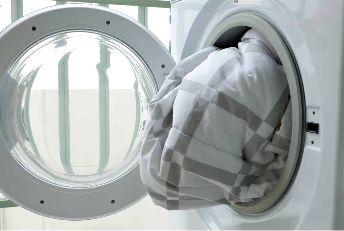 checkered white and grey duvet half way in a front loader washing machine