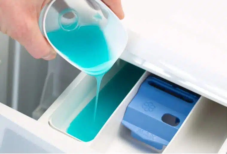 man pouring blue laundry detergent into a front loader washing machine