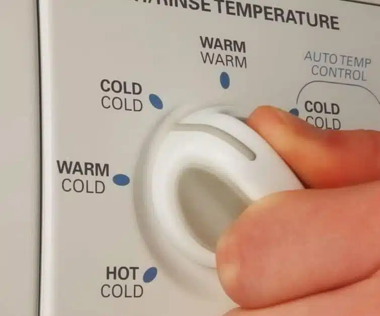 person turning water temperature dial on a washing machine