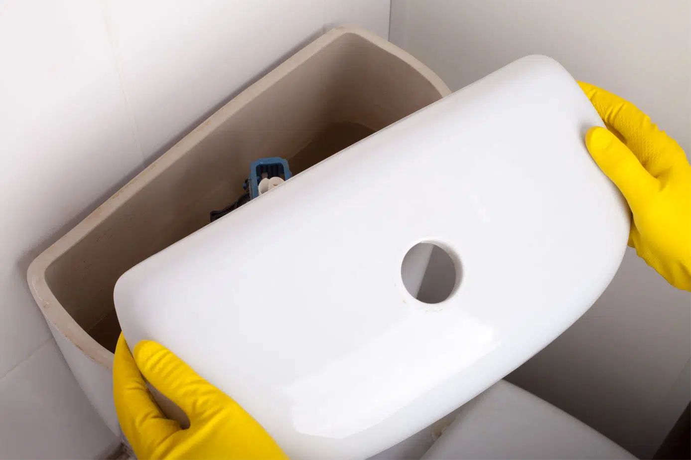 person wearing yellow gloves lifting up lid of toilet tank