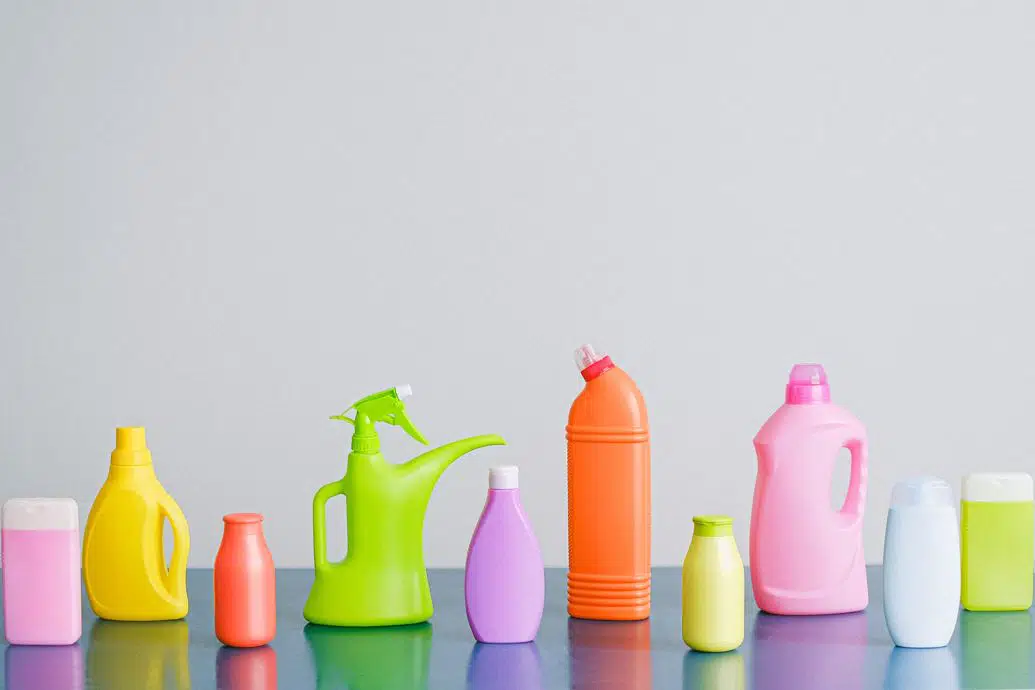 ten bottles of miscellaneous different coloured cleaning products on a blue benchtop