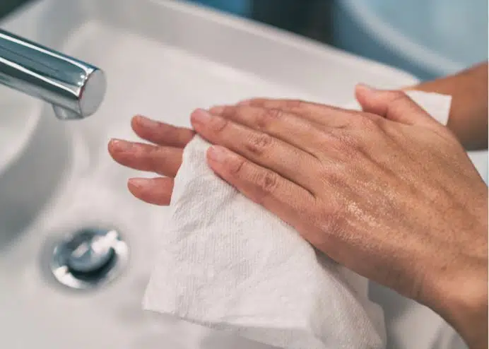 woman wiping hands with sanitise wipes in front of bathroom basin