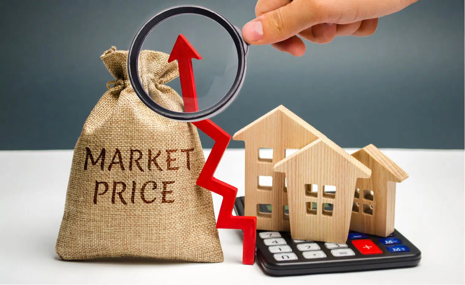 a man holding a magnifier over three wooden block houses on an large calculator next to a sandbag that says market price