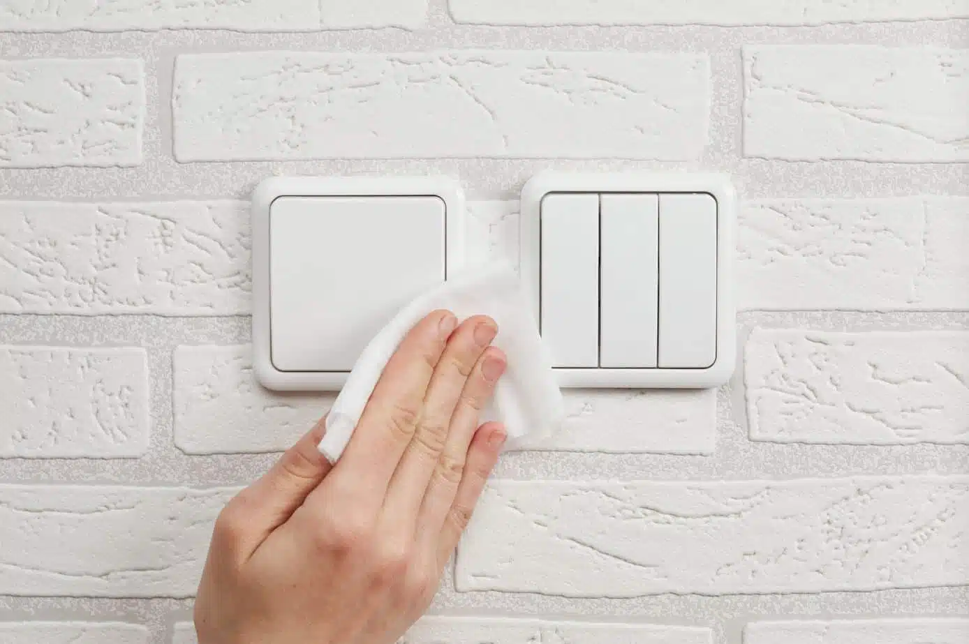 front view of person wiping down light switches with a disinfectant cloth