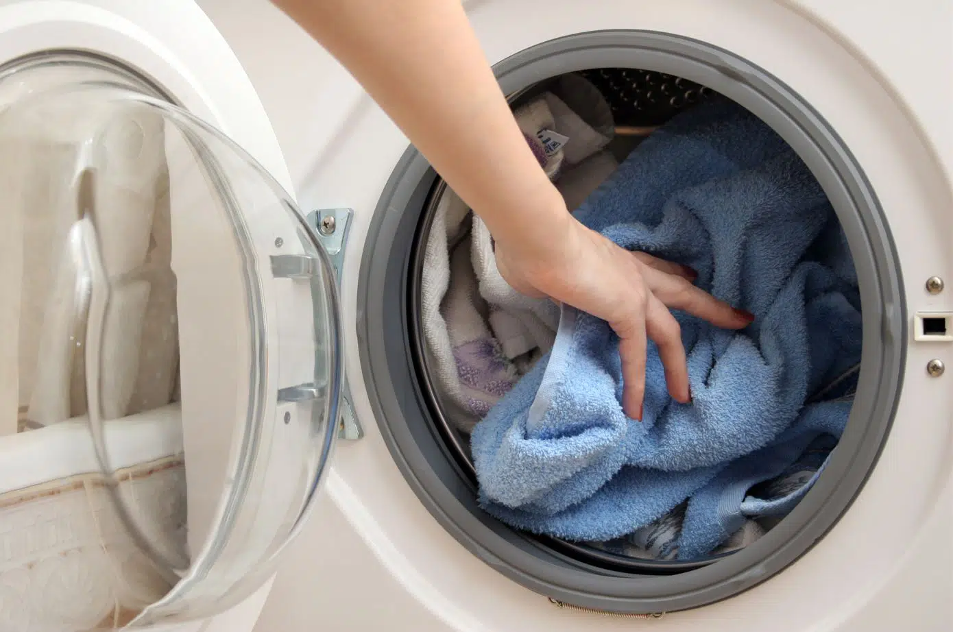 person placing blue bath mat into a full white front loader washing machine