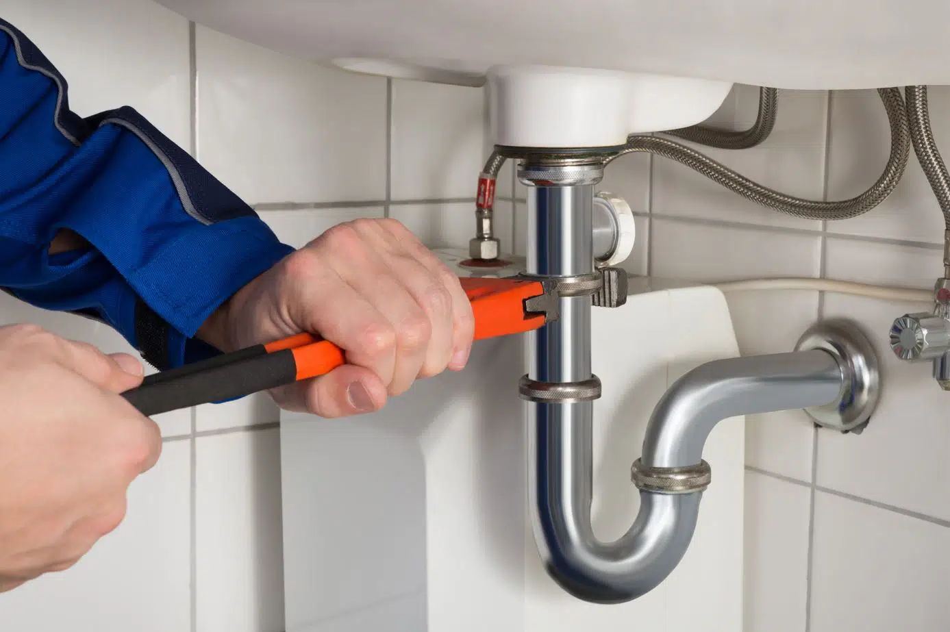 plumber using orange wrench to tighten stainless steel drain pipe under bathroom sink