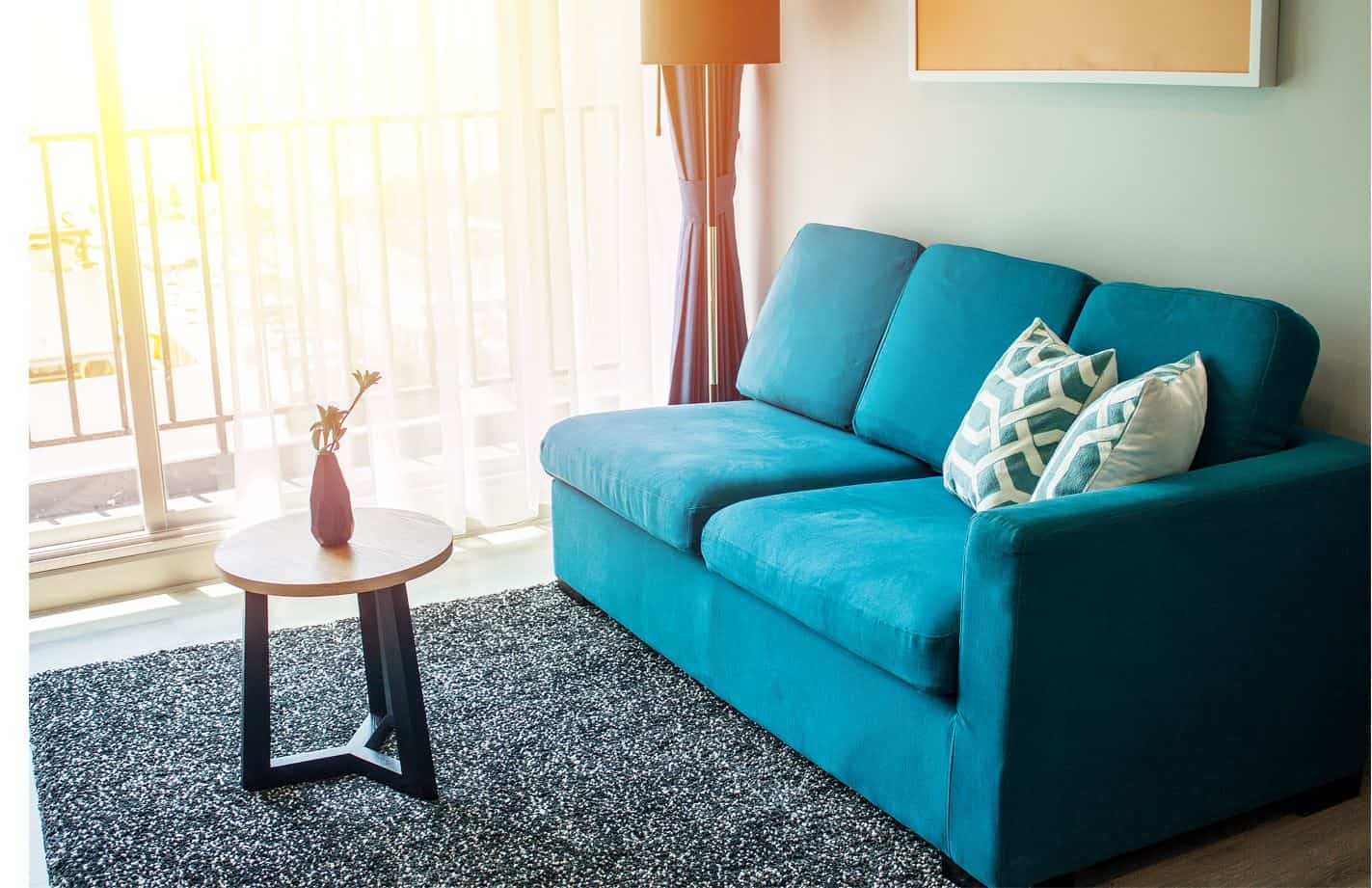 three seater blue upholstered couch in small sunlit living room