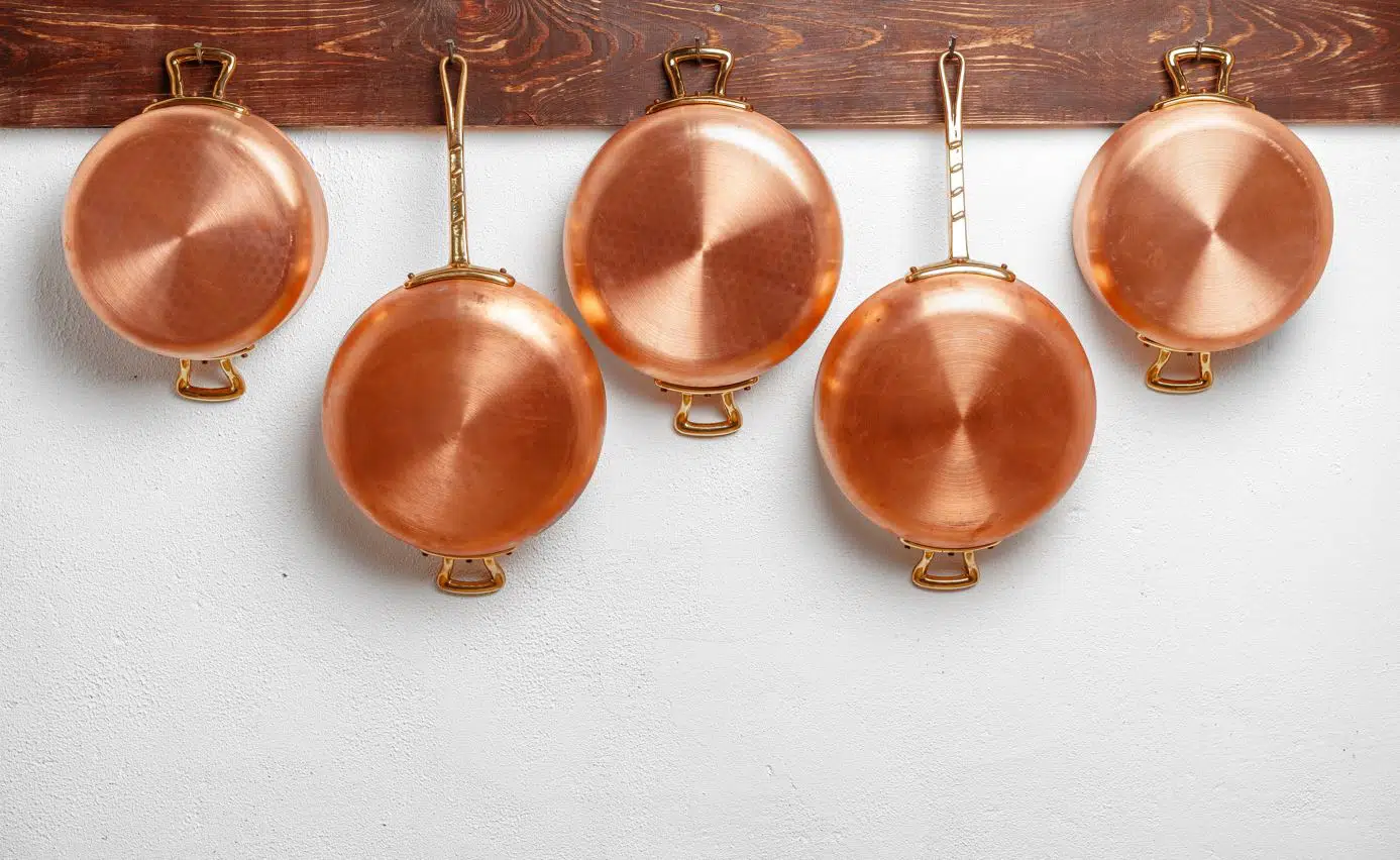 five copper pots hanving from a wooden board