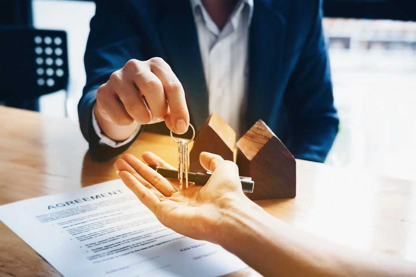seated real estate wearing a blue suit agent passing a set of house keys to a tenant 