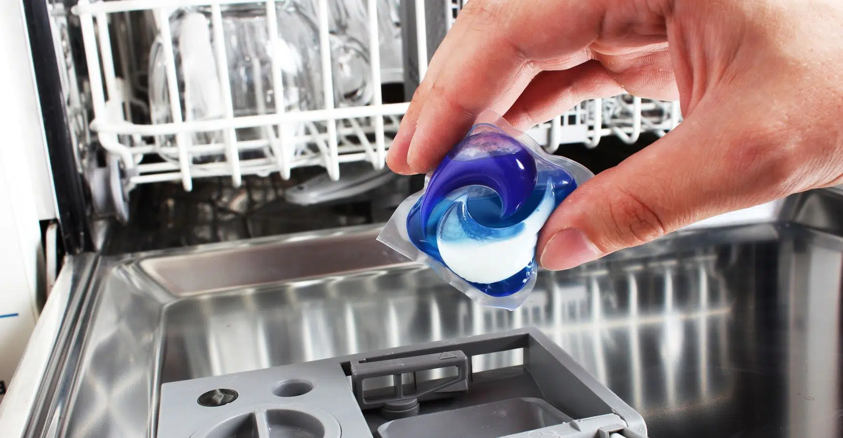 man holding dishwashing pod over dishwasher pod capsule