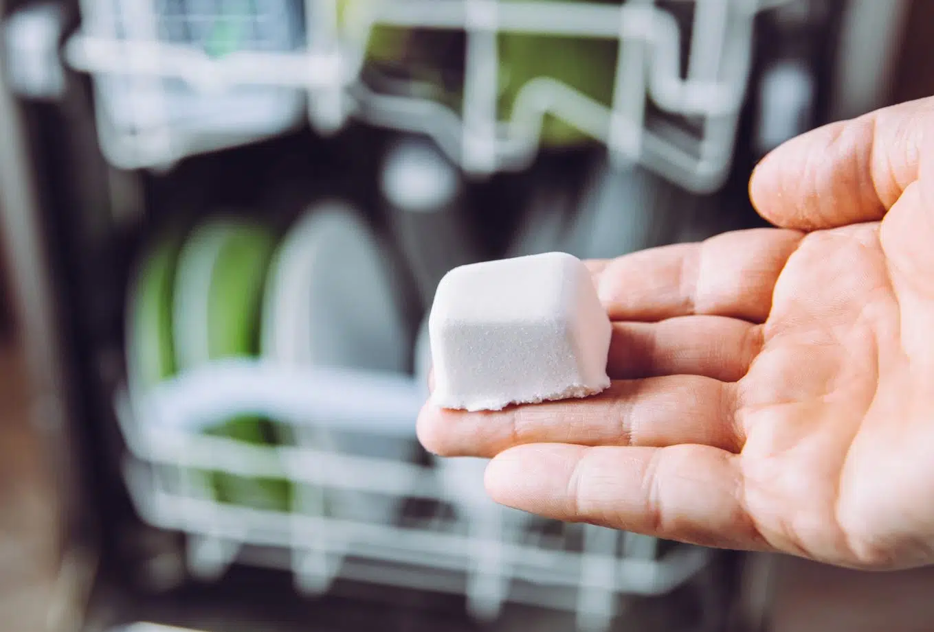 man in front of opened dishwasher holding all natural dishwasing pod