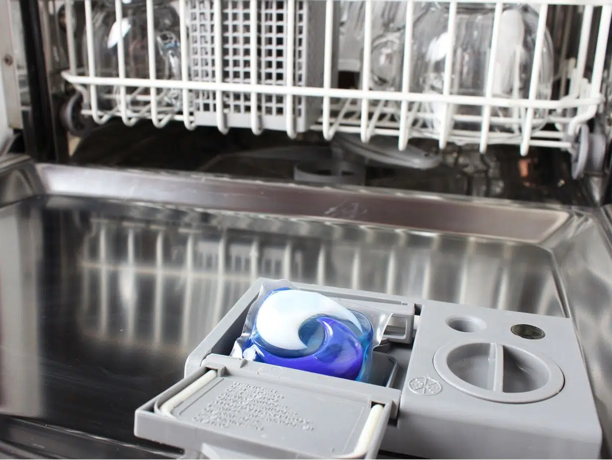 opened half filled chrome dishwasher with dishwasher pod in exposed pod chamber