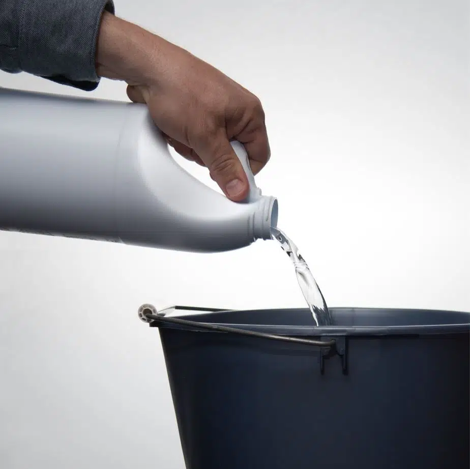 man pouring bleach into a large black bucket