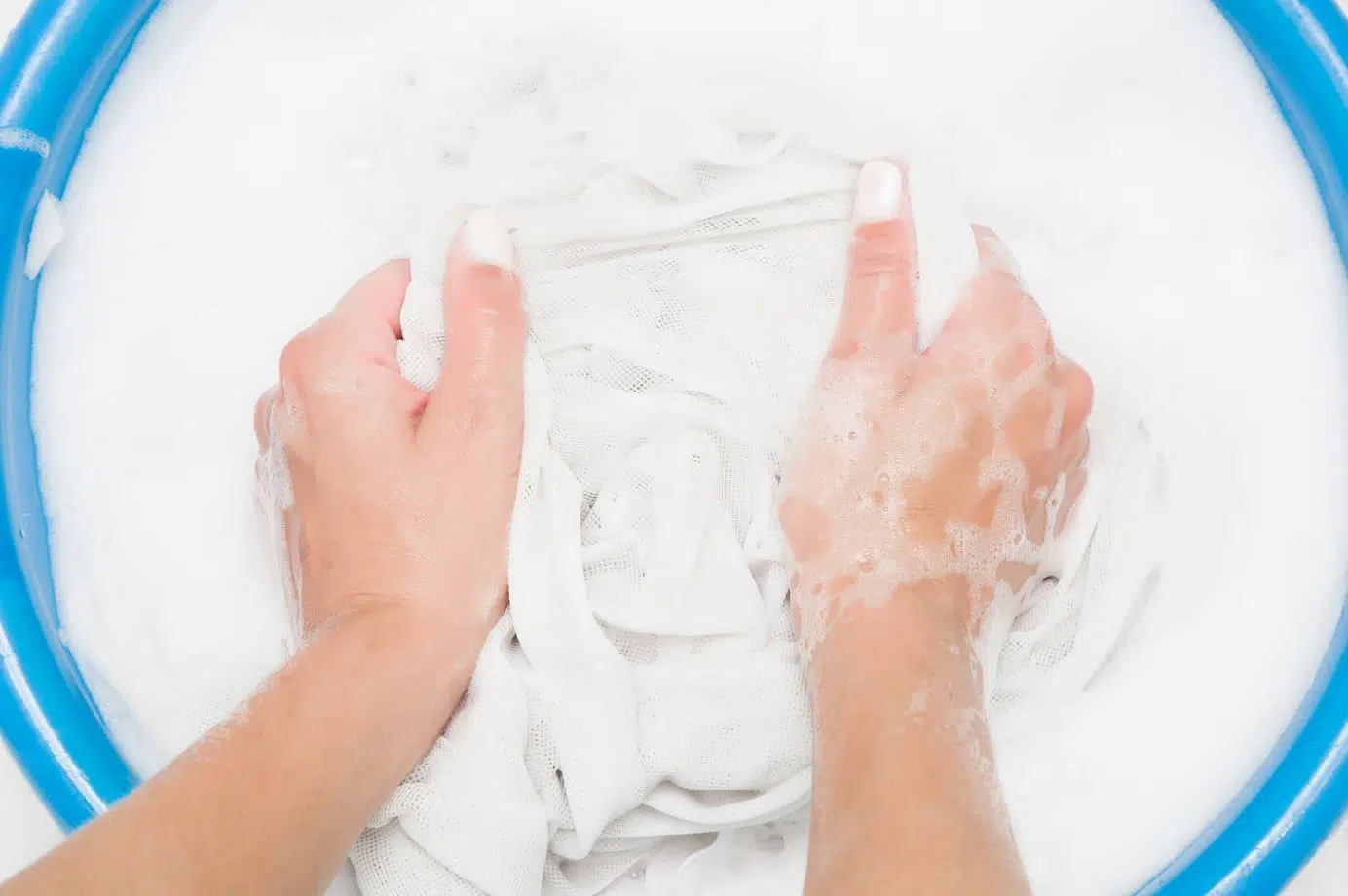 woman handwashing white curtains in a large blue tub